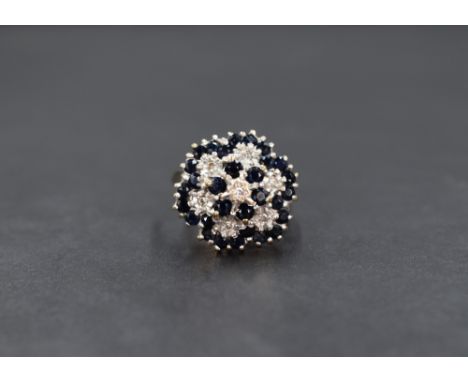 A 9ct gold sapphire and diamond cluster ring, the central illusion set diamond with a six round cut sapphire surround, with t