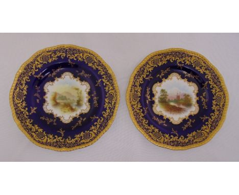 A pair of Coalport X2289 dessert plates signed by E O Ball, decorated with landscapes surrounded by cobalt blue and gilded bo