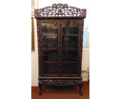 A Chinese rectangular hardwood glazed double door display cabinet, profusely carved and pierced with prunus blossom, flowers 