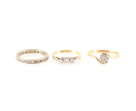 Two diamond rings and an eternity ring, a diamond three stone ring, the brilliant cut stones claw set in a yellow and white m