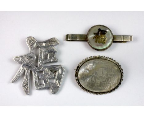 A Chinese sterling silver brooch with a white metal mounted carved mother of pearl brooch and a silver tie clip.