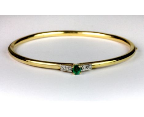 An 18ct yellow gold bangle set with an emerald and 4 diamonds.