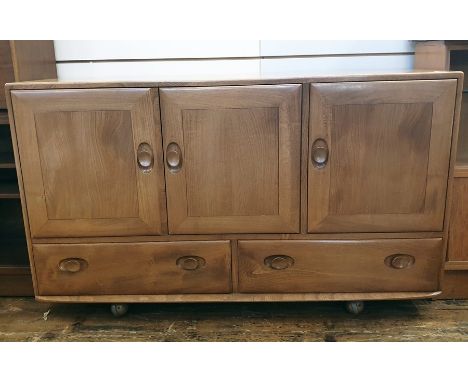 Light elm Ercol sideboard of three cupboard doors above two drawers, the whole raised on castors, 129cm x 76cm 