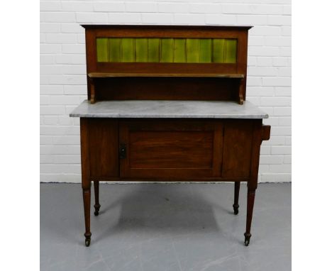 An oak Art Nouveau washstand with green tiled frieze over a single shelf and grey marble top, above a cupboard base raised on