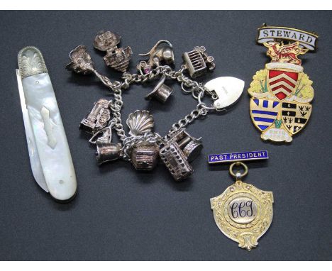 A modern silver charm bracelet containing a wide array of charms; together with a silver gilt lapel badge; a further gilt met