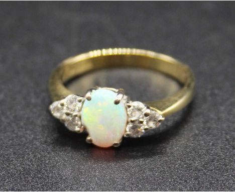 An 18ct gold, opal and diamond dress ring, arranged as a cabochon opal measuring approx 7 x 5.5mm, flanked to either side wit