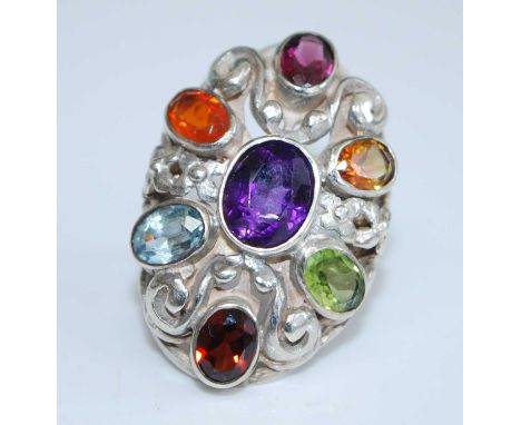 A sterling silver multi-stone dress ring, having a centre oval faceted amethyst bezel set within an open scrollwork mount wit