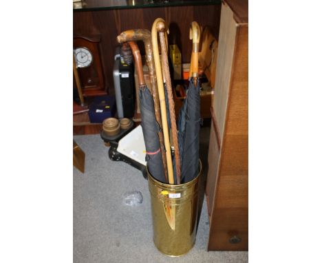 A BRASS WALKING STICK STAND CONTAINING VINTAGE UMBRELLAS, CARVED WALKING STICKS ETC