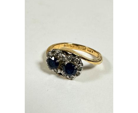 An 18ct gold two stone sapphire cross over ring, each circular cut sapphire is approximately .25ct, surrounded by white metal