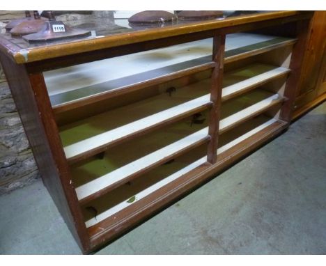 A vintage haberdashery shop display counter of rectangular form with inset plate glass top with fixed segmented open shelves 