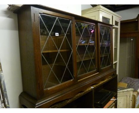 A low and slender freestanding oak bookcase enclosed by three leaded light rectangular panelled doors revealing segmented adj