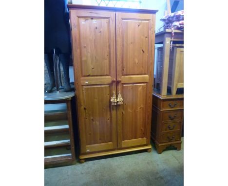 A small modern stripped pine wardrobe enclosed by a pair of twin moulded panelled doors with simple shelf and hanging rail to