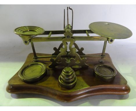 A vintage brass assembly of postage scales with graduated circular weights, all supported on a shaped timber base