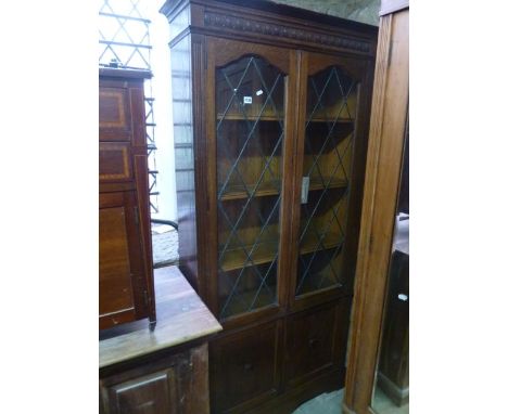A 1920s oak freestanding bookcase enclosed by two pairs of panelled doors, the upper with glazed leaded light panels revealin