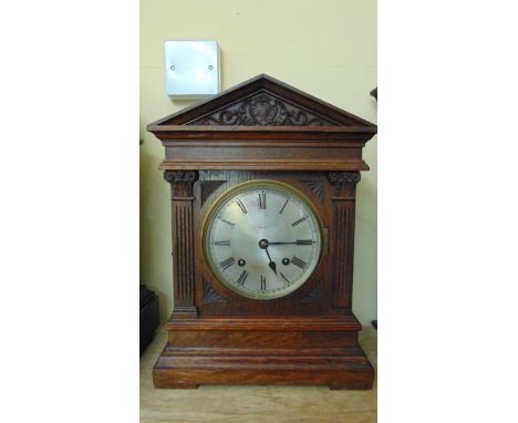 An Edwardian oak bracket clock in the classical style with ionic column supports beneath an architectural cornice, with silve
