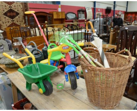 A childs push along trike, a child's wheel barrow, wicker basket, childrens garden tools and a Raffles Hotel umbrella 