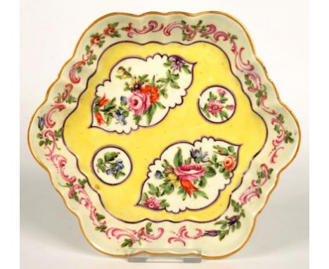 A WORCESTER YELLOW GROUND TEAPOT STAND, PAINTED WITH PANELS OF FLOWERS, THE TRAILING PUCE SCROLL BORDER WITH FLOWERS AND FOLI