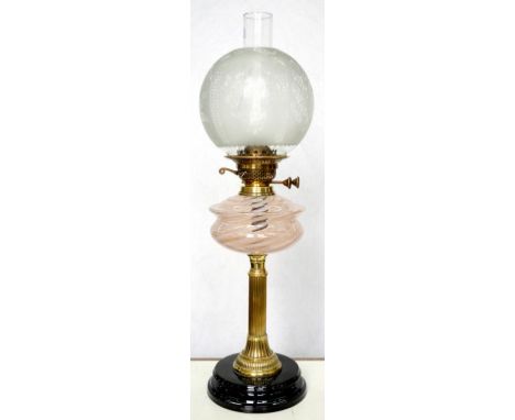 AN EDWARDIAN BRASS OIL LAMP, THE REEDED SHAFT ON BLACK GLAZED POTTERY FOOT, PALE PINK AND CLEAR SPIRALLY DECORATED GLASS FOUN