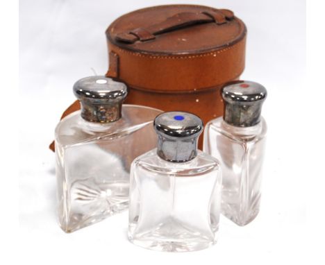 Set of three late Victorian glass spirit flasks, the silver tops with enamel roundels contained in a cylindrical leather carr