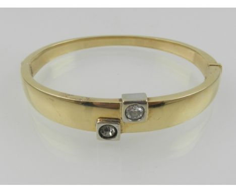 A yellow metal and white metal mounted hinged bangle, set two white gemstones, the clasp stamped 585.  