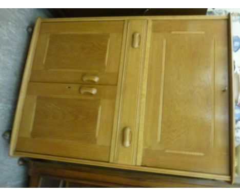 An Ercol honey coloured oak cocktail cabinet, the top having round corners, over a lockable fall front, enclosing an illumina