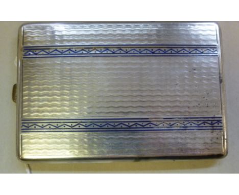 A French silver coloured metal folding cigarette case with engine turned and patterned blue enamelled decoration, on a button