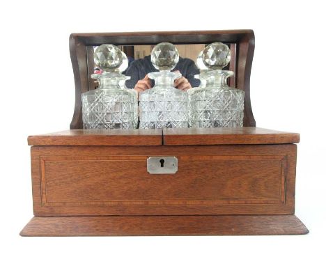 An Edwardian mahogany, marquetry and satinwood banded tantalus having three cut glass decanters with mirror behind and foldin
