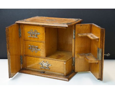 Early 20th Century oak smokers cabinet housing a pipe rack with three drawers behind a twin door cabinet with armorial crests