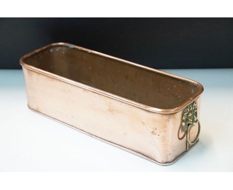 Copper rectangular copper planter with rolled rim, rounded ends and brass lion mask and drop ring handles, 40cm long x 12cm h