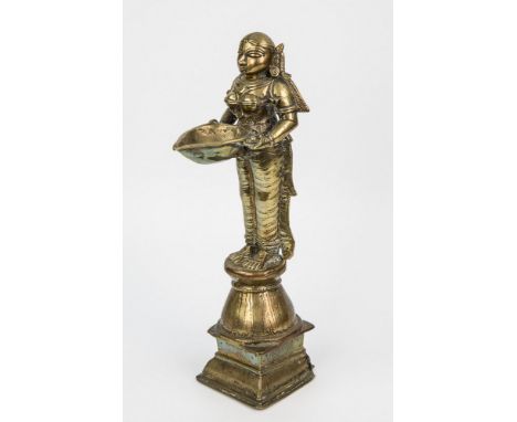 A brass Indian oil lamp 19th century, in the form of Lakshmi the Hindu Goddess, standing upright on a waisted plinth, proffer