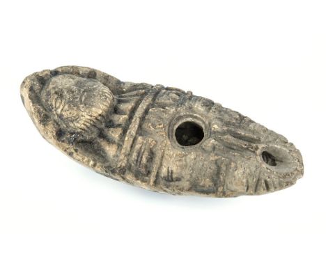An ancient Syrian pottery oil lamp oval form with rounded base, bearded figure serving as the ansa with relief carved decorat
