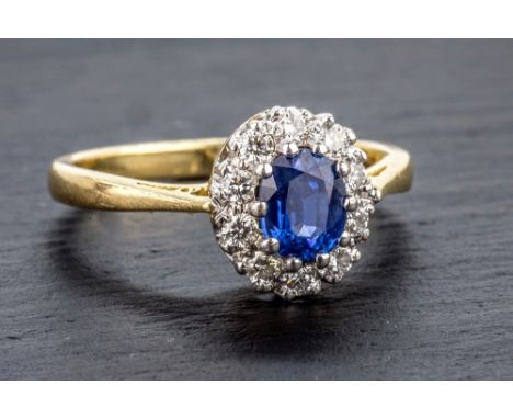 An 18ct yellow gold, sapphire and diamond cluster ring the oval cut light blue sapphire within a border of twelve 0.02 carat 