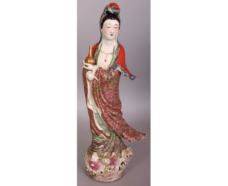 A LARGE CHINESE FAMILLE ROSE PORCELAIN FIGURE OF GUANYIN, holding a sprinkler vase and standing on a peach, lotus and wave fo