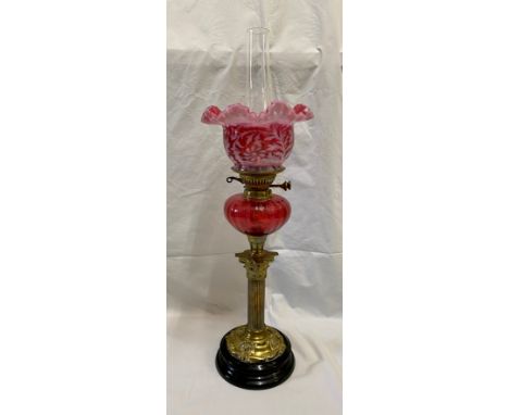 A 19thC cranberry glass oil lamp with cranberry and white glass shade, Corinthian brass column and slate base. 70cms h.Condit