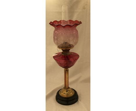 A Victorian cranberry glass oil lamp with brass column and slate base and an acid etched cranberry glass shade. 58cm h to top