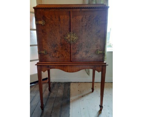 A burr walnut drinks cabinet with pull out shelf and revolving circular drinks holder to interior, with brass strapping and h