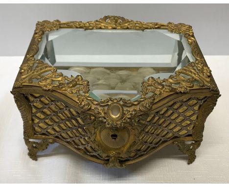 A decorative gilded metal jewellery box with bevelled glass panels, cherubs and foliage design and a cushion lined interior a