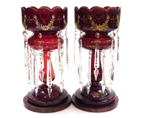 A pair of late 19thC ruby glass lustres, with floral enamel decoration, and prismatic cut glass drops, raised on wooden bases