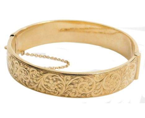 A 9ct gold bangle, with floral and foliate engraving, monogram engraved, on a snap clasp with safety chain as fitted, 16.1g  