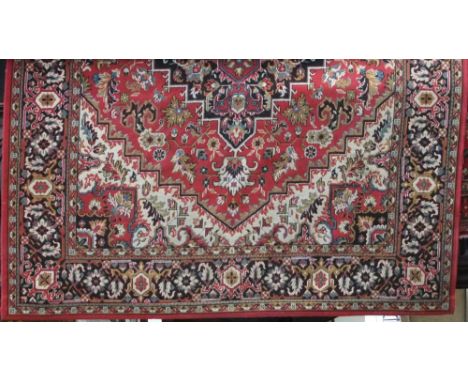 Hammadan style machine woven carpet with central navy blue floral medallion and further floral scrolls upon a red ground, 350