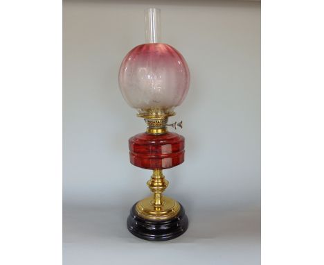 Late 19th century cast brass oil lamp with faceted cranberry glass reservoir, upon a turned column and stepped circular base,