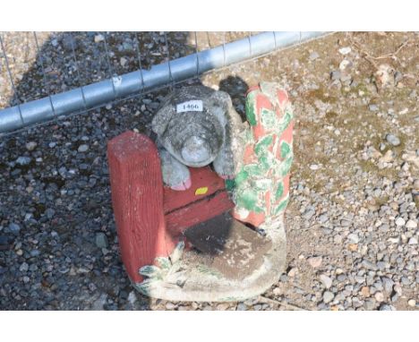 A cast concrete and painted garden ornament in the form of a pig over a field gate inscribed 'the grass is greener'