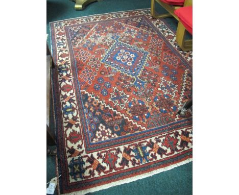 A PERSIAN WOOL RUG the wine, blue and beige ground with central serrated panel and stylized flowerheads within a three strand