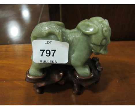 A JADE FIGURE modelled as a foo dog shown standing on a hardwood base 7cm (h) x 5cm (w) x 9cm (l)