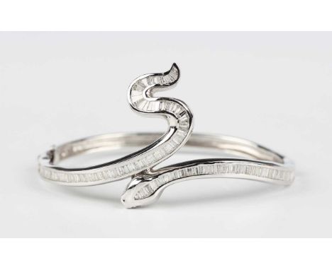 A white gold and diamond oval hinged bangle in a serpentine design, mounted with baguette cut diamonds, detailed ‘K18 218’, t