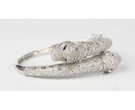 A silver, colourless and blue gem set panther bangle in a crossover design, each terminal formed as a panther’s head with blu