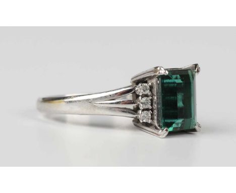 A platinum ring, claw set with a rectangular step cut green tourmaline between diamond three stone shoulders, detailed ‘Pt 90