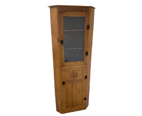 'Gnomeman' adzed oak corner cupboard, fitted with one lead glazed door enclosing two loose shelves over one panelled door wit