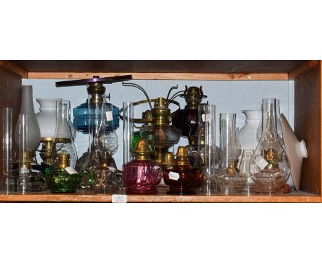 A quantity of Victorian and later oil lamps and chamber lamps including coloured glass examples and a quantity of spare chimn