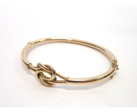 A HINGED BANGLE in yellow precious yellow metal, unmarked, with a lovers knot motif, 9.9g gross, cased and boxed